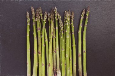 Siyah arka planda taze çiğ yeşil kuşkonmaz mızrakları. Sağlıklı sebzeler, vejetaryen yemekleri ve yemek pişirme konsepti için malzemeler. Kapat, boşluğu kopyala.