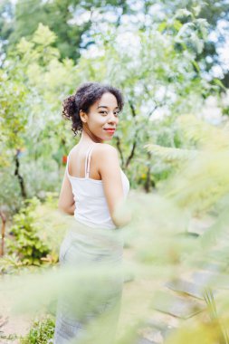 Beyaz tişörtlü, parkta ya da açık havada yaşayan Afro-Amerikalı genç bir kadın. Bahar ya da yaz mevsimi