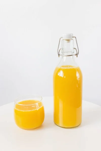 Fresh squeezed orange juice in bottle and glass on table, white background. Healthy beverage for breakfast. Side view, copy space