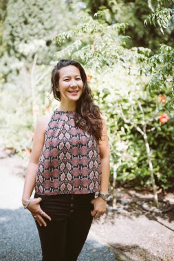 Yaz parkında kot pantolon ve gömlek giymiş güzel, mutlu, çok kültürlü bir Japon kadın, gülümsüyor.