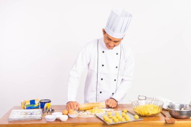 Aşçı ceketi giyen erkek şef, izole arka planda ahşap merdane kullanıyor.