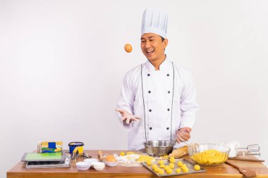 Erkek aşçı yumurta fırlatırken mutfak masasında yalıtılmış arka planda hamur yapıyor.