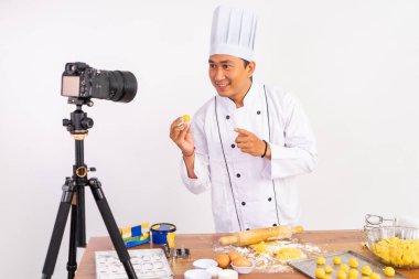 Şef, şef ceketi giyip, masada çatal bıçakla kek hamuru yaparken özel bir video hazırlıyor.