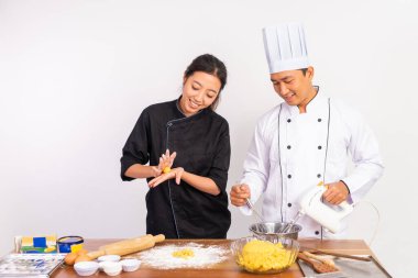 İki aşçı birlikte çalışarak izole edilmiş arka planda bir masada kurabiye hamuru yapıyorlar.
