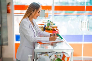 Eczacı kadın eczanede kalem ve panoyla yazı yazıyor.