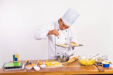 Erkek şef, izole edilmiş arka planda kek tepsisinin üzerine rendelenmiş peynir serpiyor.