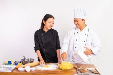 Erkek ve kadın aşçılar kurabiye hamuru yapıyorlar ve izole edilmiş arka planda mikser kullanıyorlar.