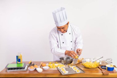 Erkek aşçı rendeleyici kullanırken peyniri izole edilmiş arka planda tepside pastaya rendeliyor.