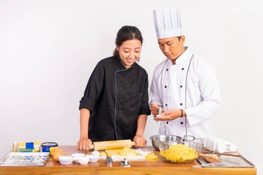 Erkek ve kadın aşçılar masada kurabiye hamurunu inceltmek için merdane kullanıyorlar.