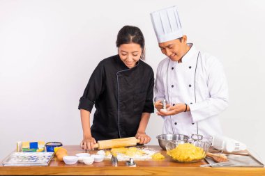 Erkek ve kadın aşçılar, izole arka planda hamur yazdırırken merdane kullanırlar.
