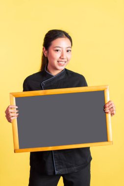 Sırıtan Asyalı kadın şef, arka planda boş tahtayı tutuyor ve gösteriyor.