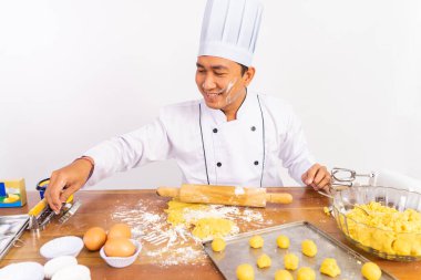 Gülümseyen erkek aşçı, kendini beğenmiş yüzüyle soyutlanmış arka planda pasta yapıyor.