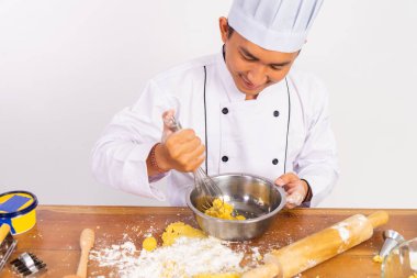 Erkek şef karışık kasede çırpıcıyı ayrı bir arka planda, masada kullanıyor.