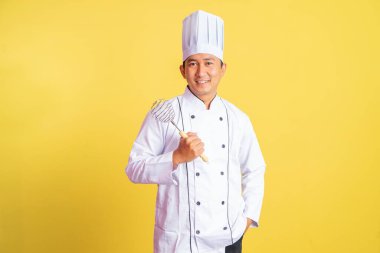 Yakışıklı, şef ceketi giyen erkek şef çırpıcıyı tutarken izole bir zeminde duruyor.