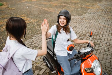 Öğrenci kız kask takıyor motosiklet sürerken arkadaşıyla el çırpıyor.