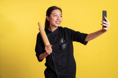 Asyalı kadın şef gülümserken selfie izole arka planda ahşap raptiye tutuyor.