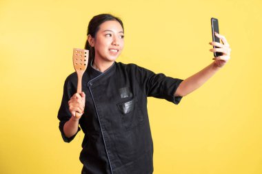 Kadın şef selfie izole edilmiş arka planda cep telefonu ve el ele tutuşma spatulası kullanıyor