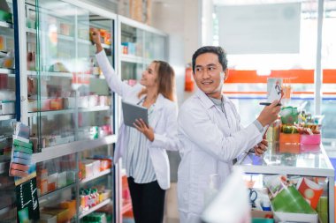 Eczanedeki arkadaşlarıyla konuşurken üniformalı bir erkek eczacı pencereye bakıyor.