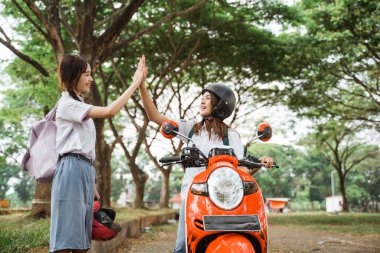 Öğrenci kız kask takıyor. Arkadaşını motosikletle eve götürürken el çırpıyor.