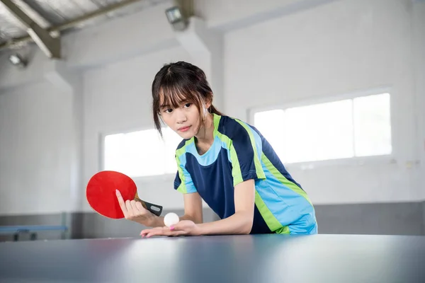 Close up of a female athlete holding a paddle and a ball ready to serve in a ping pong match