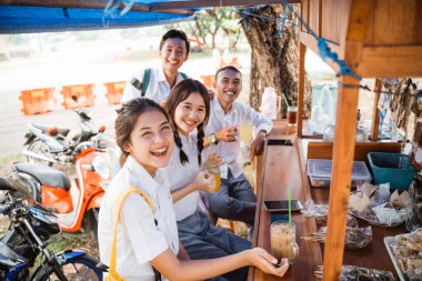 Üniformalı bir grup lise öğrencisi kameraya gülümserken tezgahta buz içiyorlar.