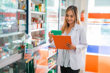 Eczacı kadın eczanede pano tutarken ilaç paketini gözlemleyerek uyuşturucu içeriğini kontrol edecek