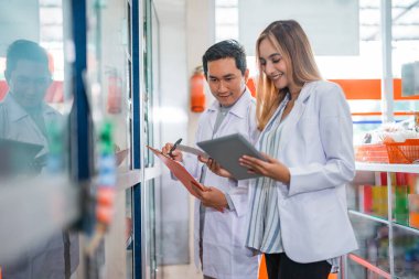 Üniformalı kadın eczacı eczanedeki arkadaşlarına sorarken tablet kullanıyor.