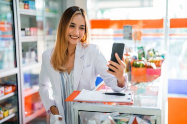 Eczanede çalışırken cep telefonu kullanan Asyalı kadın eczacı.