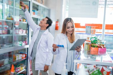 Üniformalı Asyalı kadın eczacı eczanede ilaç kontrolü için ped kullanıyor.