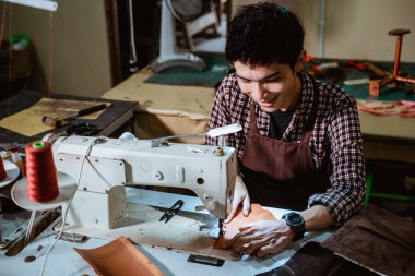Terzi dikiş masasında lambalı dikiş makinesi kullanıyor.
