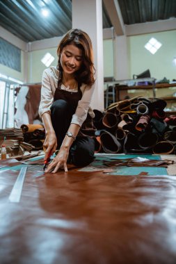 Asyalı zanaatkar kadın deri arka planda deri kesiyor.