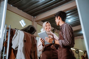 Duvak takmış bir kadın ve esnaf esmer bir geçmişe karşı tablet kullanırken sohbet ediyorlar.