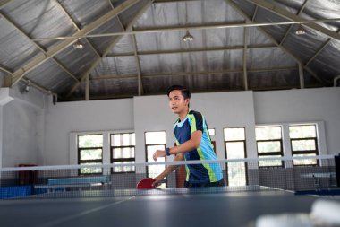 Asyalı erkek sporcu ping pong maçında topu almaya hazır.