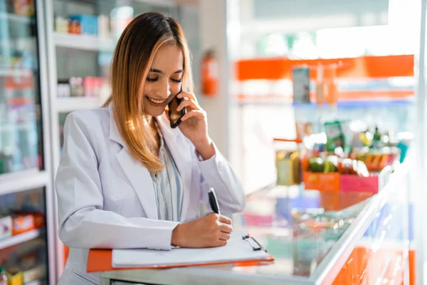 female pharmacist receives call from customer and writes drug name request on paper