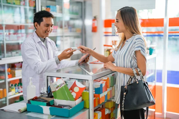 male pharmacist accepts credit card for cashless payment from female customer at pharmacy
