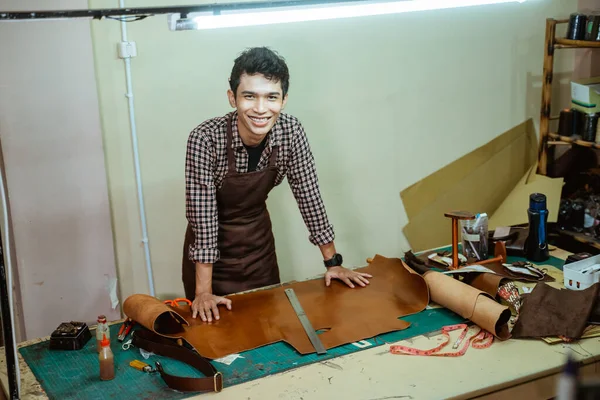 Young asian man smiling at work making patterns from leather at work