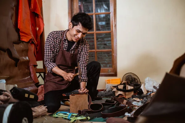 craftsman making holes in leather belts with a hammer in a leather tanning workshop
