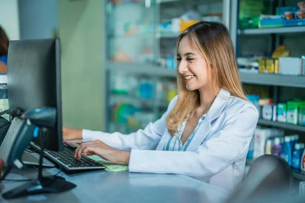 beautiful asian pharmacist in uniform working using computer in pharmacy