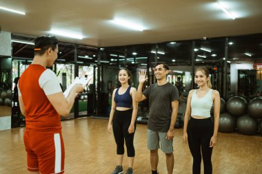 Spor salonunda çalışmadan önce grup toplantısına liderlik eden Asyalı erkek eğitmen.