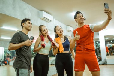 Asyalı erkek eğitmen ve genç spor grubu selfie 'si spor merkezinde akıllı telefon kamerasıyla birlikte.