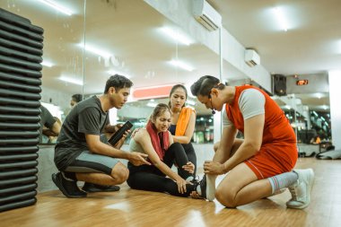 Erkek eğitmen, bir kadın spor salonunda egzersiz yaparken bacağını incittiğinde yardımcı olur.