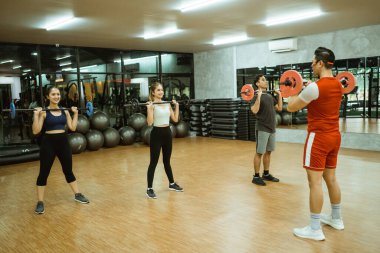 Erkek eğitmen ve genç spor grubu spor salonunda beden eğitimi sırasında halter kullanıyor.