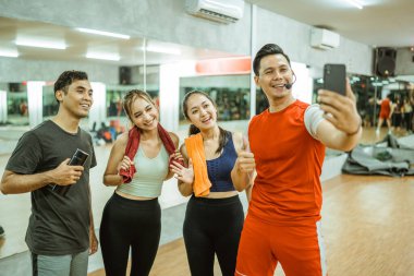 Asyalı erkek eğitmenle selfie ve spor salonunda akıllı telefonlu genç bir grup.