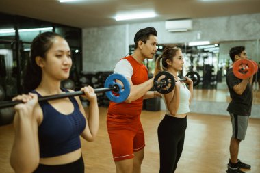 Erkek eğitmen, halter kullanırken genç bayana omurga pozisyonu hakkında talimat verir.