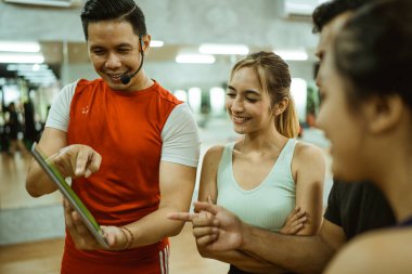 Güzel bir kadının yanında spor salonunda antrenman yaparken atletik gençlere ekranı gösteren bir eğitmen.