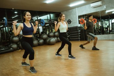 Genç spor grubu spor salonunda antrenman sırasında koltuk değnekleriyle çömelme hareketleri yapıyor.