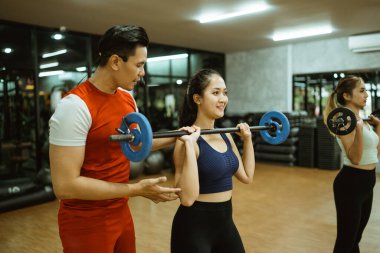 Erkek eğitmen spor salonunda halterle genç Asyalı kadını eğitiyor.