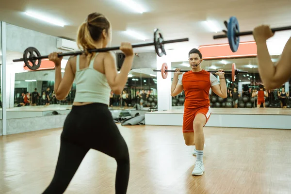 selective focus instructor doing back squat barbell in front of young women during body combat training