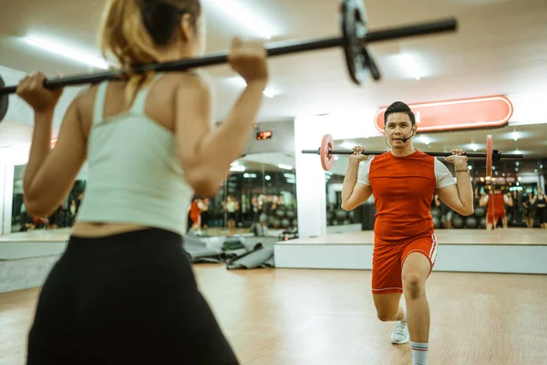 selective focus instructor lifting barbell in front of young woman during body combat training