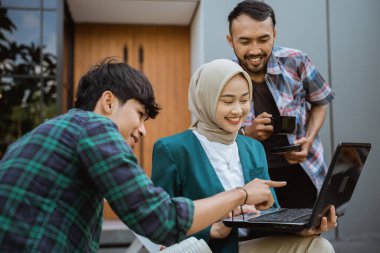 three college students using and looking at laptop in cafe